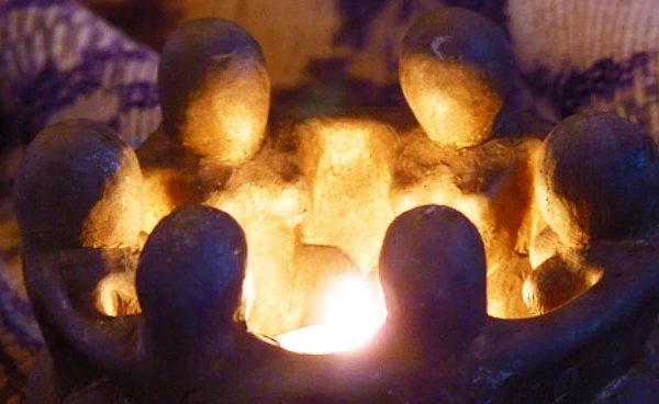 A candle holder formed by six figures with their arms around each other, surrounding a flame in the center.