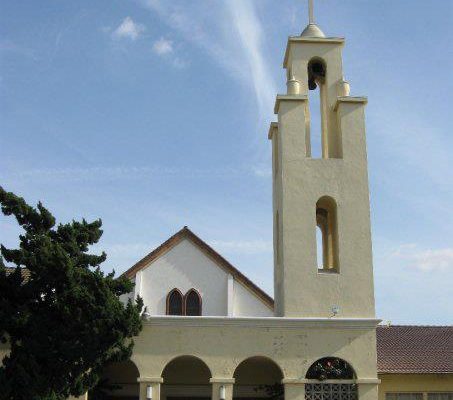 The steeple and front of First Christian Church Pomona, a pale tan building with numerous archways, on a sunny day.