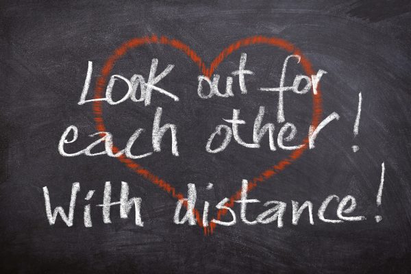 Over top of a red outline of a heart are the words, "Look out for each other! With distance!" written in white chalk.