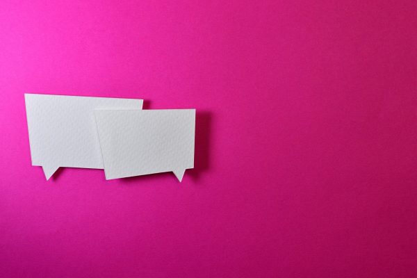 2 white paper cutouts of question bubbles against a hot pink background.