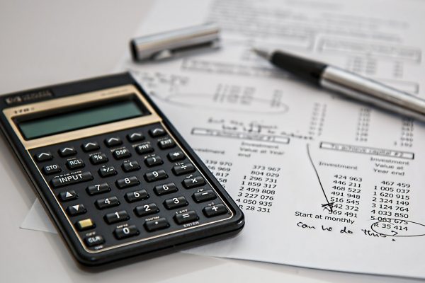 A black calculator sits besides an uncapped pen and a financial statement that has been scribbled upon.