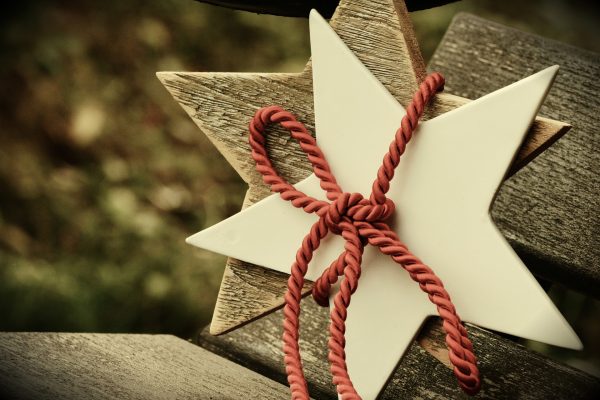 A white ceramic five-pointed star is stied over a wooden five-pointed star with a thick red cord.