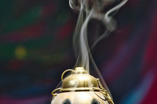 The smoke of incense wafts out from various openings in a golden censer. Image via Pixabay.