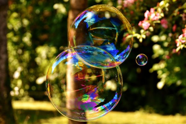 Two large soap bubbles and a third smaller bubble shimmer in the sunlight. Image by Here and now, unfortunately, ends my journey on Pixabay from Pixabay.