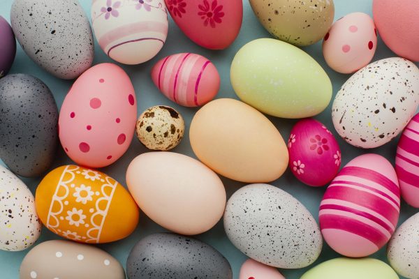 An assortment of Easter eggs against a gray background. The eggs are all different sizes and are decorated with a variety of bright and pastel colors. Image via Pixabay.