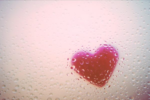A pink heart is seen from the other side of a clear glass, covered in water droplets. Image via Pixabay.