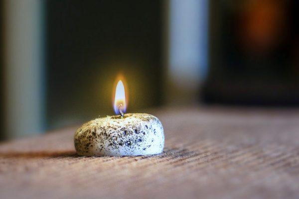 A small black and white speckled candle is lit on a ridged brown surface.