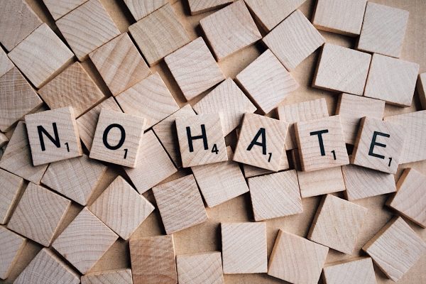 Light brown Scrabble tiles spelling out, "No Hate" are arranged atop similar tiles, but with their blank sides facing up. Image via Pixabay.