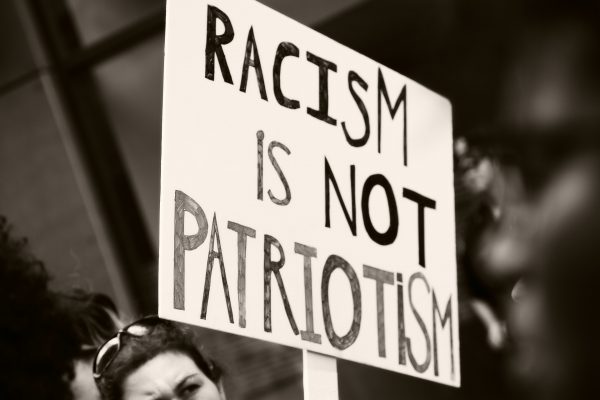 A black and white photo of someone holding a sign that reads, "Racism is Not Patriotism".