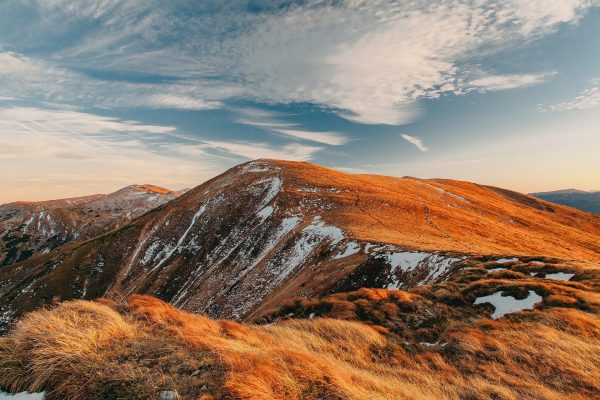 Rolling mountains are covered intermittently with snow and orange-red grass.