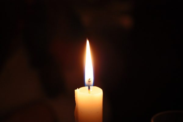 A single white taper candle is lit in a dark room. Image via Pixabay.
