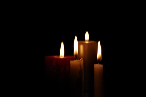 Four candles of various sizes, heights, and colors are lit in a dark room. Only the two candles in the foreground are in focus. They are cream-colored taper candles. The candles in the background are wider and colored red and gold. Image via Pixabay.