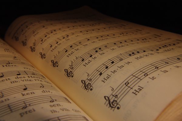 An up-close picture of an open hymnal. The upper right corner of the hymnal is dark; several lines of a “Hallelujah” chorus are visible on the righthand page. Image via Pixabay.