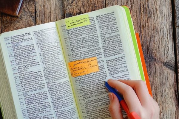 A person studies a well-marked Bible, using colored highlighters to underline important verses on a wooden table.