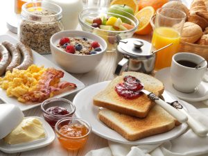 A breakfast spread with toast and jam, coffee, eggs and bacon, cereal and fruit.