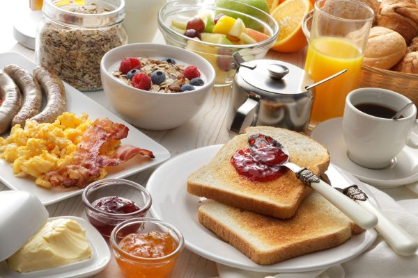 A breakfast spread with toast and jam, coffee, eggs and bacon, cereal and fruit.